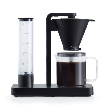 A PERFORMANCE BLACK coffee maker with a transparent water reservoir and a glass carafe filled with coffee. Featuring unique technology for the perfect temperature, it boasts two award badges: one with a laurel wreath indicating "Best i Test Tek.no" and another that reads "Testvinner" with stars and a ribbon symbol.