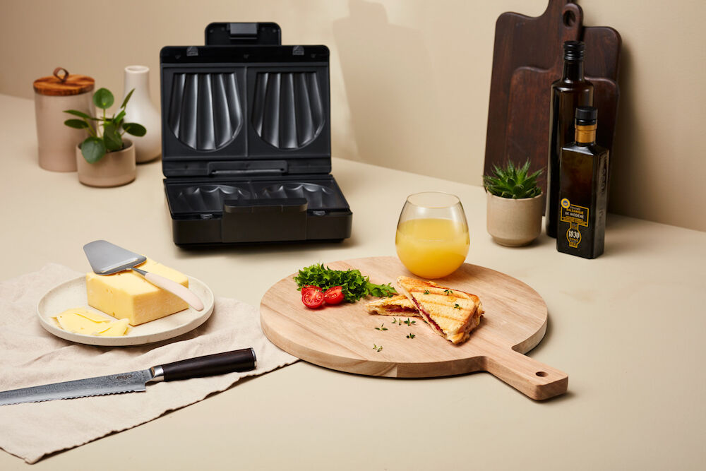 Un appareil à sandwichs ouverts EASY MELT doté de deux compartiments de cuisson triangulaires, avec des surfaces striées et de grandes plaques chauffantes pour griller. L'appareil est noir, doté d'un revêtement antiadhésif, d'une poignée sur le dessus et d'un cordon d'alimentation à l'arrière.