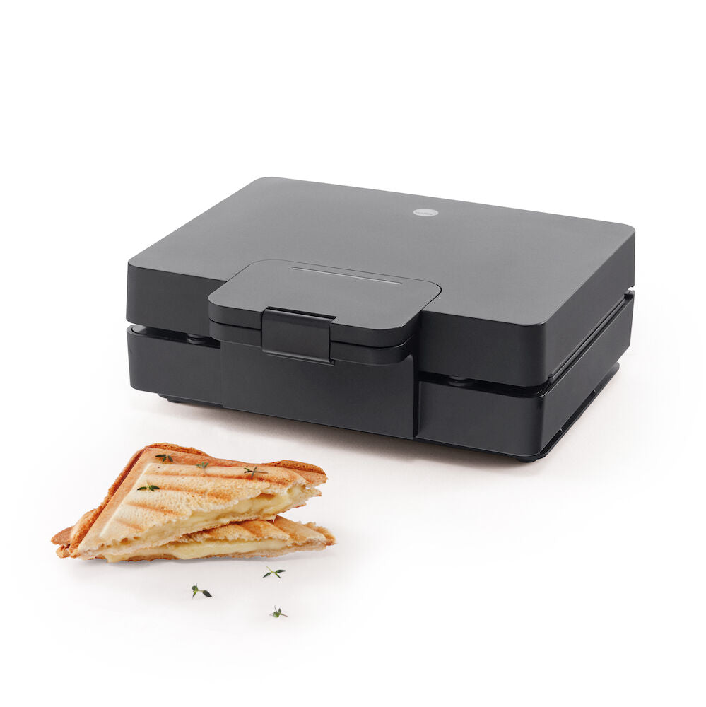 Una sandwichería EASY MELT con dos compartimentos triangulares para cocinar, con superficies estriadas y placas calefactoras grandes para asar. El aparato es de color negro, con un revestimiento antiadherente, un asa en la parte superior y un cable de alimentación en la parte trasera.
