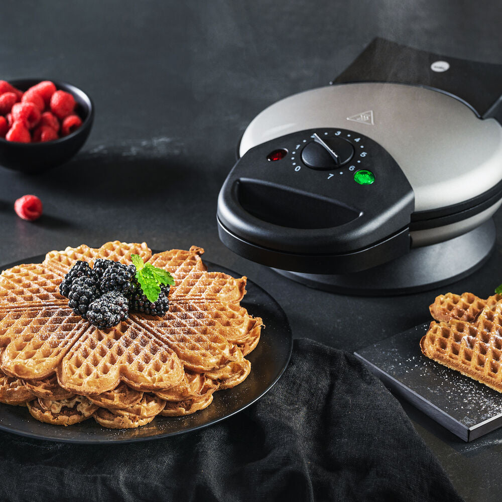 A BELL 23 with a black base and control dial. Featuring an adjustable thermostat for perfect waffles every time. Beside it are three award badges: a blue and teal circular badge reading "ANBEFALT TEK.NO," and two star-shaped badges reading "TESTVINNER" and "TESTVINNARE.