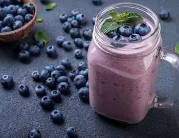 Blueberry smoothie in a glass jar with mint, surrounded by fresh blueberries