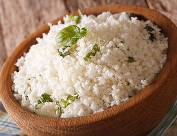 Wooden bowl of cauliflower rice garnished with fresh herbs