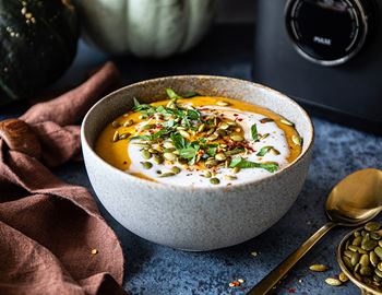 Bowl of Thai pumpkin soup topped with coconut milk, herbs and pumpkin seeds