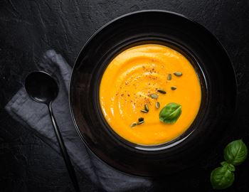 Bowl of orange pumpkin soup with pumpkin seeds and basil