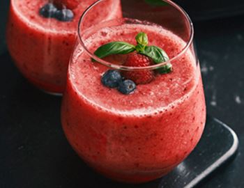Two glasses of red berry smoothie topped with fresh berries and basil leaves