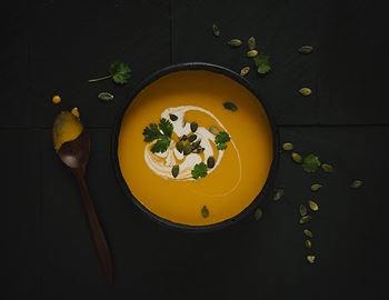 Bowl of carrot and ginger soup topped with coconut cream, herbs and pumpkin seeds