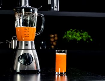 Glass of carrot juice beside the Wilfa Xplode Vital blender