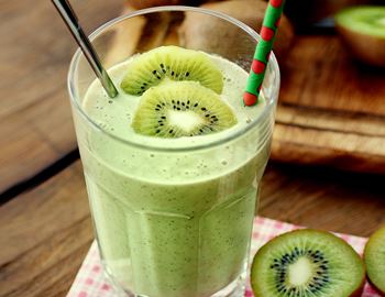Kiwi smoothie in a tall glass topped with kiwi slices and a striped straw