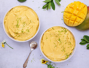 Two bowls of mango nice cream topped with lime zest and fresh mango