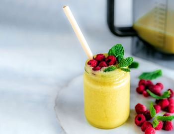 Yellow mango slush in a glass with mint and raspberries