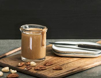 Jar of homemade nut butter on a wooden board with nuts