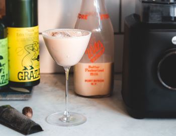 Glass of creamy vegan oat liqueur beside a Wilfa blender