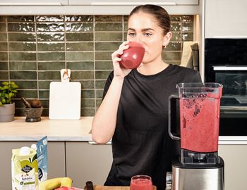 Woman drinking a red smoothie in a kitchen beside a Wilfa blender