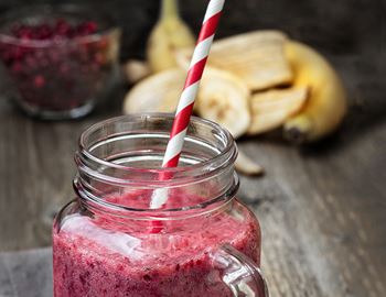 Red lingonberry smoothie in a glass jar with striped straw and banana