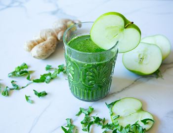 Green kale smoothie in a glass with apple slices and fresh ginger