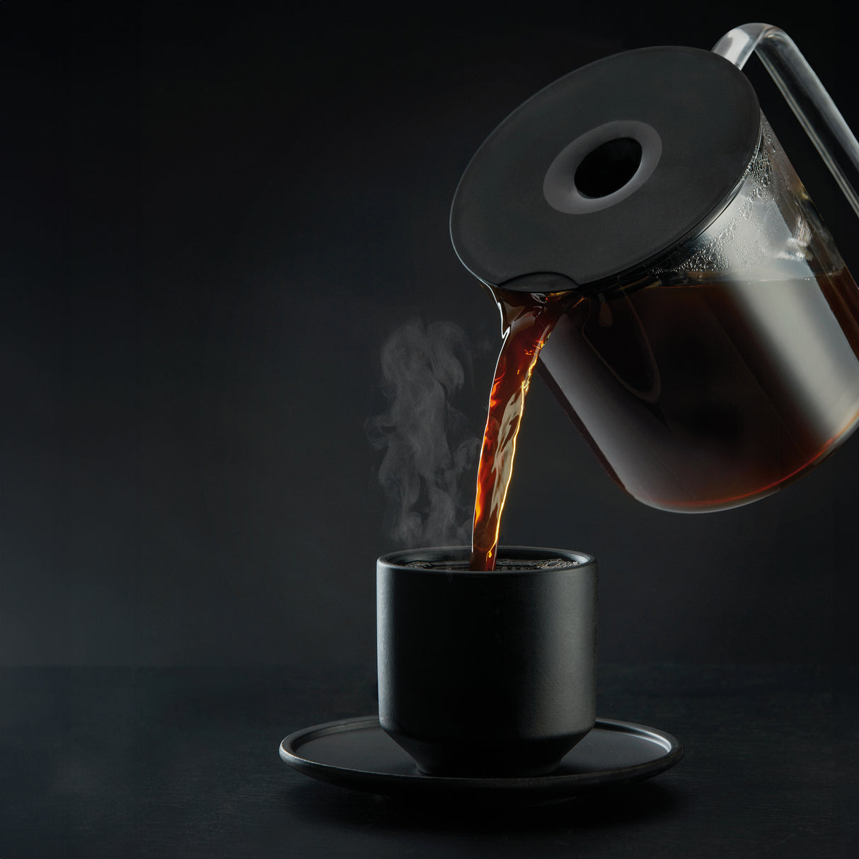A PERFORMANCE BLACK coffee maker with a transparent water reservoir and a glass carafe filled with coffee. Featuring unique technology for the perfect temperature, it boasts two award badges: one with a laurel wreath indicating "Best i Test Tek.no" and another that reads "Testvinner" with stars and a ribbon symbol.