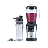 A stainless steel sports blender with a transparent pitcher filled with blueberries, spinach, and other fruits. Next to it is an ACTIVLIFE STEEL 2go bottle containing a dark purple smoothie topped with a secure lid. A small bunch of blueberries and a couple of mint leaves are placed nearby.
