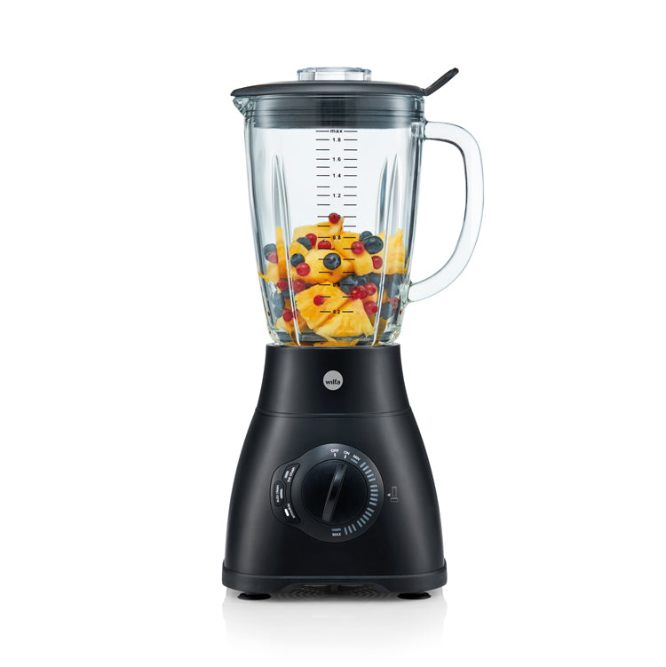A powerful XPLODE 1500 AUTO BLACK, filled with chopped mangoes, blueberries, and strawberries. The clear glass container has measurement markings and a black lid. Featuring a 1500 W motor, various control settings, a speed dial, and an automatic cleaning program for effortless maintenance.